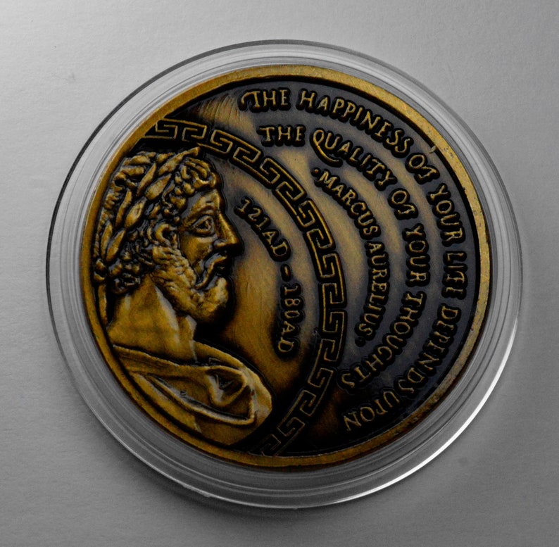 May include: A gold-colored coin with a profile of a man on one side and an inscription that reads "THE HAPPINESS OF YOUR LIFE DEPENDS UPON THE QUALITY OF YOUR THOUGHTS - MARCUS AURELIUS 121AD - 180AD" on the other side.