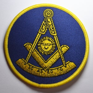 May include: A yellow embroidered Masonic symbol on a blue background. The symbol is a square and compass with a sun in the centre.