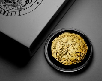 May include: A gold-colored coin with a skeletal figure holding a spear and a Latin inscription that reads "MEMORARE NOVISSIMA TUA".