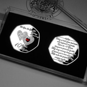 Puede incluir: Moneda conmemorativa plateada en una funda transparente. La moneda presenta un diseño de corazón y el texto "10 Years Together". Presentada sobre un fondo negro.