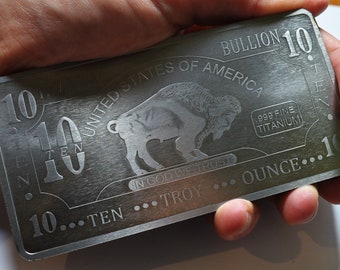 May include: A silver-coloured 10 ounce titanium bullion bar with an image of a buffalo and the text "United States of America" and "In God We Trust".