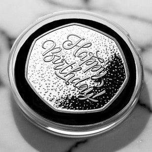 May include: A silver coin with a hexagonal shape and the words "Happy Birthday" inscribed on it.