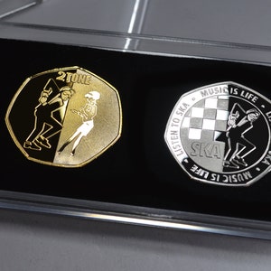 Puede incluir: Dos monedas conmemorativas de dos tonos en una caja de plástico transparente. La moneda dorada presenta una silueta en blanco y negro de dos bailarines con el texto "2TONE". La moneda plateada presenta una silueta en blanco y negro de un bailarín con el texto "LISTEN TO SKA - MUSIC IS LIFE - LISTEN TO SKA - MUSIC IS LIFE"