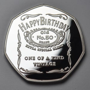 Może przedstawiać: Okrągły srebrny medal z wypukłym wzorem. Medal przedstawia napis "Happy Birthday" w ozdobnym kroju pisma, a także słowa "Old No. 50 Brand Extra Special Blend One of a Kind Vintage".