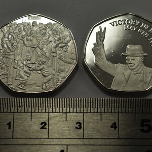 May include: A silver commemorative coin celebrating Victory in Europe Day, May 8th, 1945. One side features a crowd of people celebrating, while the other side shows Winston Churchill giving a victory salute.