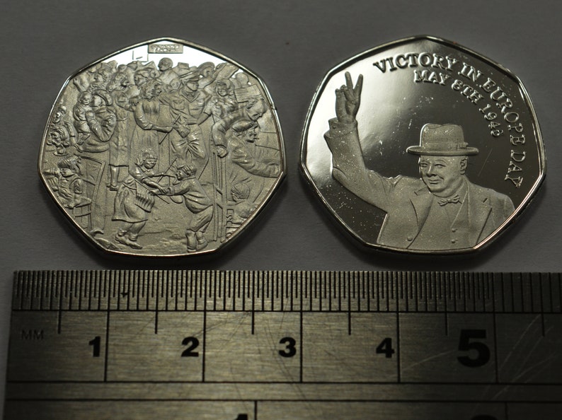 May include: A silver commemorative coin celebrating Victory in Europe Day, May 8th, 1945. One side features a crowd of people celebrating, while the other side shows Winston Churchill giving a victory salute.