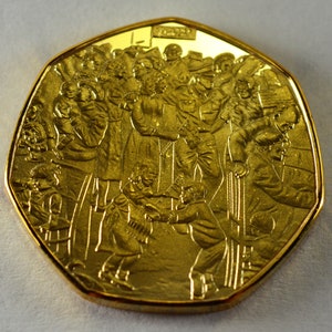 May include: A gold-colored commemorative coin featuring a detailed relief design of a crowd of people, including children, gathered together. The coin has a dodecagonal shape and the inscription "2000" is visible on the top.