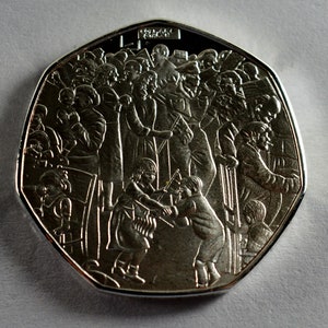 May include: A silver commemorative coin featuring a detailed design of a crowd of people, including children, with the words "One Pound" inscribed on the top.