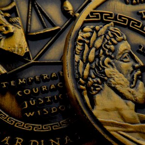 May include: Close-up of a gold-colored coin with a profile of a man with a beard and a laurel wreath on his head. The coin has a Greek key design around the edge and the words "TEMPERAT", "COURAC", "JUSTIC", "WISDO" are visible on the coin.