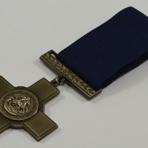 Pu&ograve; includere: Una medaglia di bronzo con un design a croce e un centro circolare che presenta una rappresentazione di un cavaliere a cavallo. La medaglia &egrave; attaccata a un nastro blu scuro.