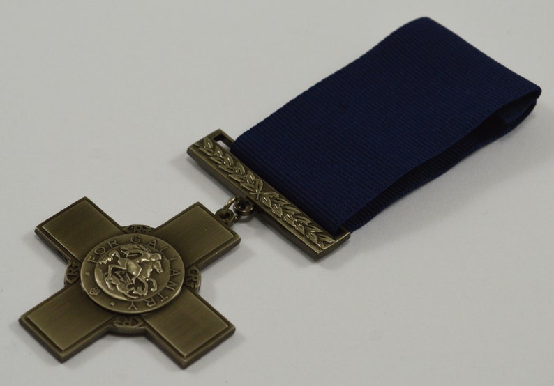 Pu&ograve; includere: Una medaglia di bronzo con un design a croce e un centro circolare che presenta una rappresentazione di un cavaliere a cavallo. La medaglia &egrave; attaccata a un nastro blu scuro.