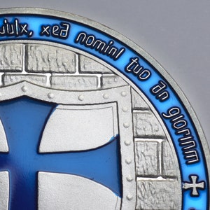 K&ouml;nnte beinhalten: Eine silberne M&uuml;nze mit einem blauen Emaille-Design. Die M&uuml;nze zeigt einen Schild mit einem blauen Kreuz und dem Text "in ulix, xed nominl tuo dn glorim".