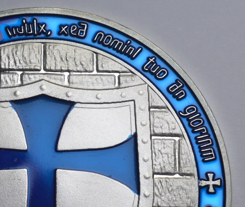 K&ouml;nnte beinhalten: Eine silberne M&uuml;nze mit einem blauen Emaille-Design. Die M&uuml;nze zeigt einen Schild mit einem blauen Kreuz und dem Text "in ulix, xed nominl tuo dn glorim".
