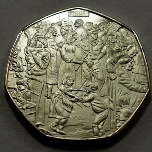 May include: A silver commemorative coin featuring a detailed design of a crowd of people gathered together. The coin has a domed shape and a raised rim.