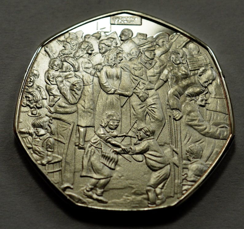 May include: A silver commemorative coin featuring a detailed design of a crowd of people gathered together. The coin has a domed shape and a raised rim.