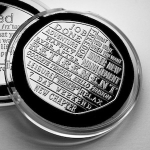 May include: A silver coin with engraved text, presented in a clear plastic case. The coin features words such as "DONE", "ADVENTURE", "RETIREMENT", and "NEW CHAPTER". The coin is set against a black velvet background.