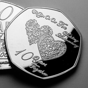 May include: Silver coin with two intertwined hearts and the text "For You Our Tin Wedding Anniversary 10 Years Together".