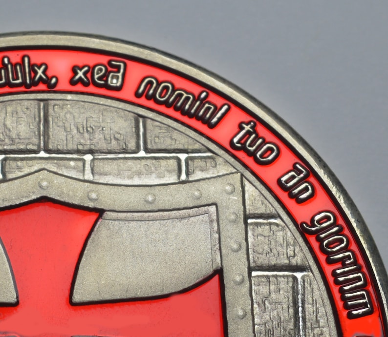 Op de afbeelding: Een zilverkleurige metalen munt met een rood en zwart ontwerp. De munt heeft een bakstenen muur met een rood schild en de tekst "dulx, xed nominl tuo dn glorium".
