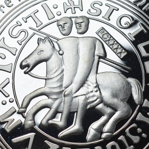 Op de afbeelding: Een zilveren munt met een gedetailleerd beeld van een ridder te paard. De ridder houdt een speer vast en heeft twee hoofden. De munt heeft de tekst "ST:H:STGL" rond de rand.