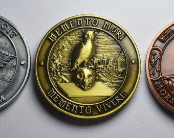 May include: Three round metal coins with different designs. The first coin is silver with an hourglass and wings, and the text "TEMPUS FUGIT CARPE DIEM". The second coin is gold with an owl and the text "MEMENTO MORI MEMENTO VIVERE". The third coin is copper with a skeleton and the text "MORS VINCIT OMNIA".