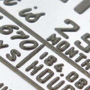 May include: Close-up of a silver metal tag with the text "252 Months is 670 Days 184.08 Hours".