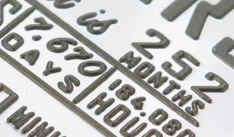 May include: Close-up of a silver metal tag with the text "252 Months is 670 Days 184.08 Hours".