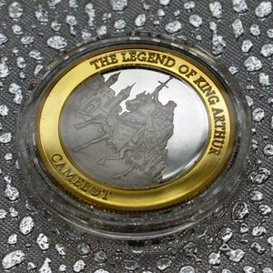 May include: A silver coin with a gold rim featuring a depiction of King Arthur and the legend "The Legend of King Arthur Camelot".