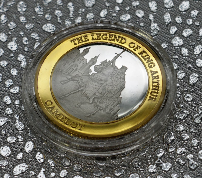 May include: A silver coin with a gold rim featuring a depiction of King Arthur and the legend "The Legend of King Arthur Camelot".