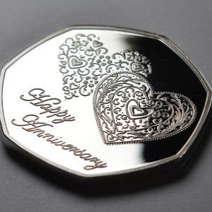 May include: A silver coin with a decorative heart design and the words "Happy Anniversary" inscribed on the front.