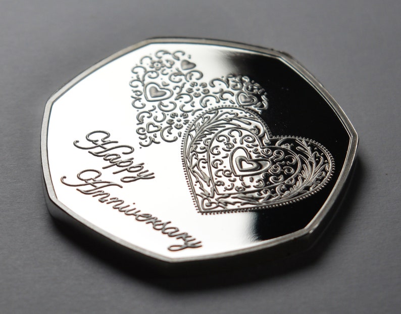 May include: A silver coin with a decorative heart design and the words "Happy Anniversary" inscribed on the front.