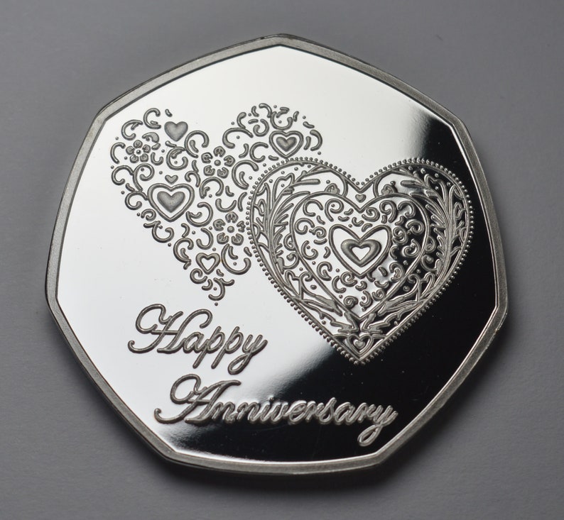 May include: Silver coin with a decorative design of two intertwined hearts and the text "Happy Anniversary".
