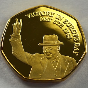 May include: Gold-colored coin commemorating Victory in Europe Day, May 8th, 1945. The coin features a portrait of Winston Churchill raising his hand in victory.