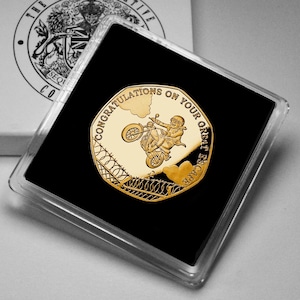 May include: A gold-colored coin in a clear plastic case. The coin features a motorcycle stunt with the words "CONGRATULATIONS ON YOUR GREAT ESCAPE". The coin is set against a black background.