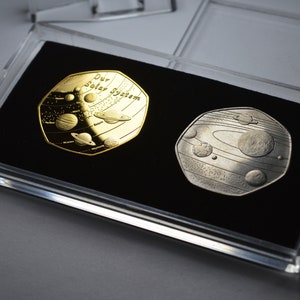 May include: Two gold and silver coins in a clear plastic case. The coins feature a design of the solar system with the text "Our Solar System" on the gold coin.