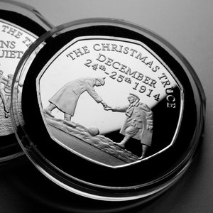 Könnte beinhalten: Eine silberne Münze zur Erinnerung an den Weihnachtsfrieden von 1914. Die Münze zeigt zwei Soldaten, die sich die Hand schütteln, mit dem Text "The Christmas Truce December 24th-25th 1914" am Rand.