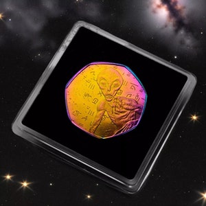May include: A gold-colored coin with a holographic finish features an alien figure with a large head and large eyes. The coin is surrounded by a black background and a starry sky.