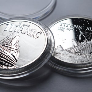 Puede incluir: Dos monedas conmemorativas de plata en estuches de plástico transparente. La moneda de la izquierda muestra el RMS Titanic navegando. La moneda de la derecha muestra el Titanic hundiéndose con el texto "TITANIC SINKS 14TH APRIL 1912."
