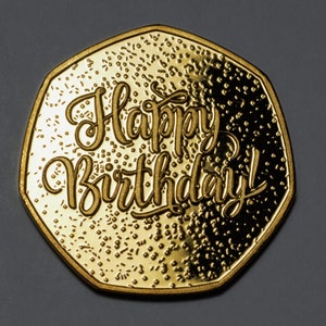 May include: A gold-coloured coin with the words "Happy Birthday!" inscribed on it.