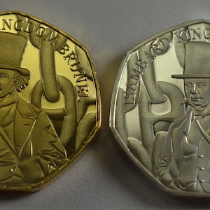 May include: Two gold and silver commemorative coins featuring a portrait of Isambard Kingdom Brunel, a British engineer. The coins are octagonal and have a raised rim.