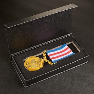 Könnte beinhalten: Eine goldene Medaille mit einem Herzdesign und der Inschrift "To My Love" in einer schwarzen Samtbox mit einem rot-weiß-blauen Band.