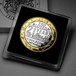 May include: A silver and gold coin with the text "You Loved for 21 Years" and the number of weeks, days, hours, and minutes in 21 years. The coin is in a black display case.