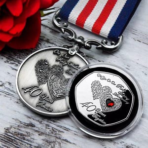 May include: Silver commemorative coin with a red jewel heart, commemorating a 40th wedding anniversary. The coin features the text "On Our Ruby Wedding Anniversary" and "40 Years Together". A red, white, and blue ribbon is attached.