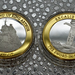 May include: Two silver coins with gold rims. The first coin features a depiction of King Arthur on horseback with the text "The Legend of King Arthur Camelot". The second coin features a sword in a stone with the text "Excalibur The Sword in the Stone".