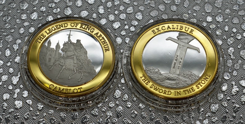 May include: Two silver coins with gold rims. The first coin features a depiction of King Arthur on horseback with the text "The Legend of King Arthur Camelot". The second coin features a sword in a stone with the text "Excalibur The Sword in the Stone".