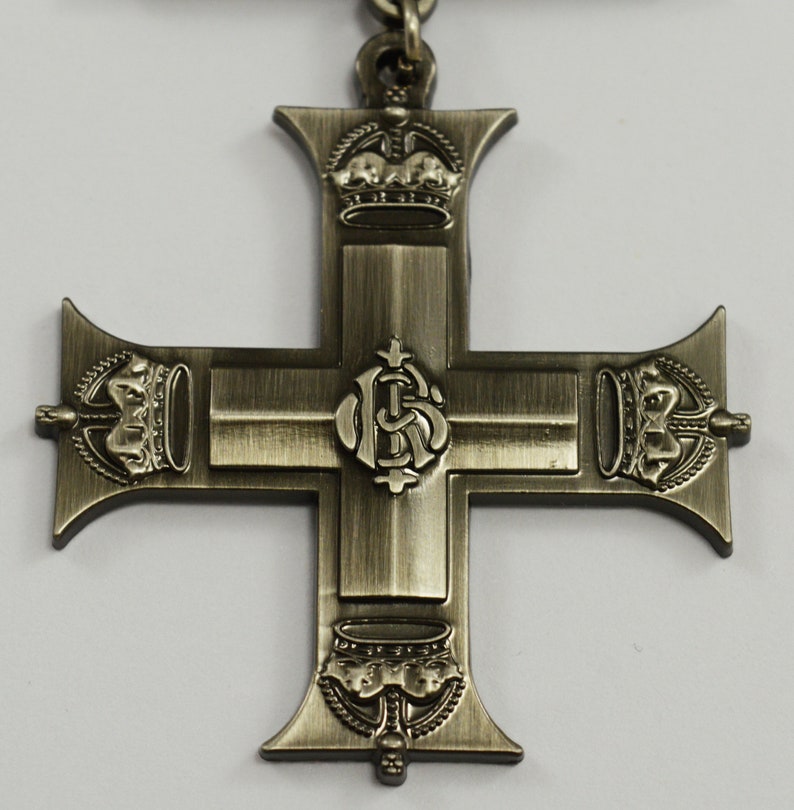Pu&ograve; includere: Una croce argentata con una corona in alto e in basso e un monogramma reale al centro. La croce &egrave; un elemento decorativo, forse per una medaglia o un premio.