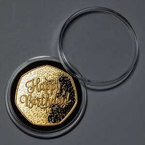 May include: A gold-coloured coin with the words "Happy Birthday!" inscribed on it. The coin is in a clear plastic case.