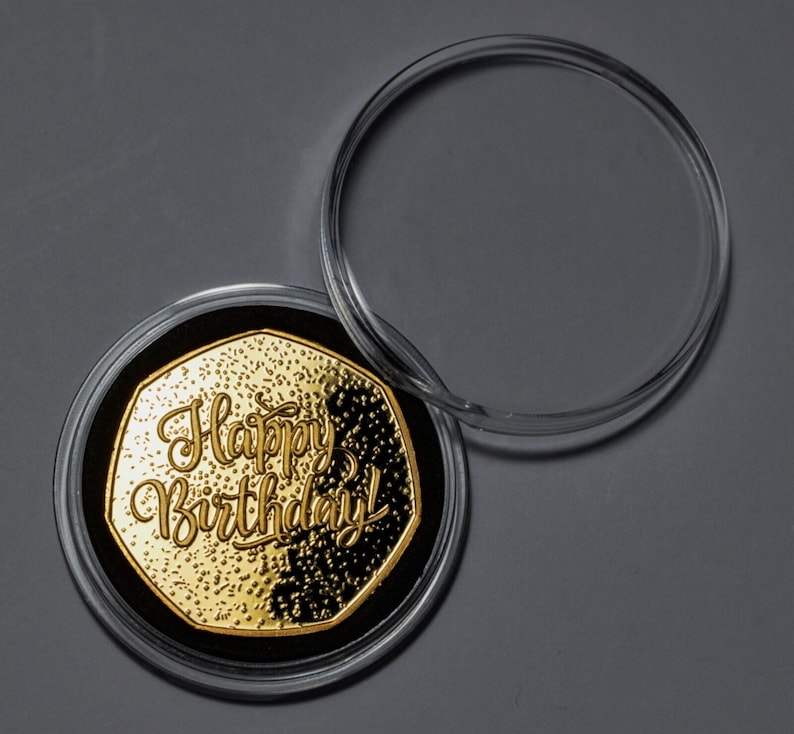 May include: A gold-coloured coin with the words "Happy Birthday!" inscribed on it. The coin is in a clear plastic case.