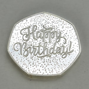 May include: Silver coin with a textured surface and the words "Happy Birthday!" inscribed in a cursive font.
