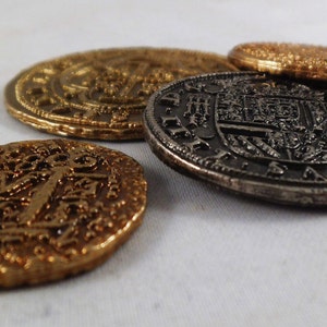 以下が含まれることがあります： 複雑なデザインと浮き彫りの文字が刻まれた、金貨2枚と銀貨2枚の計4枚のアンティークコイン。コインは白い表面に並べられています。
