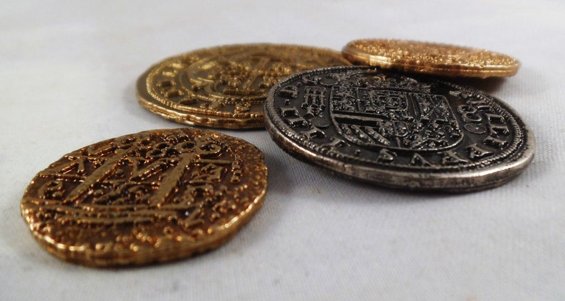 以下が含まれることがあります： 複雑なデザインと浮き彫りの文字が刻まれた、金貨2枚と銀貨2枚の計4枚のアンティークコイン。コインは白い表面に並べられています。